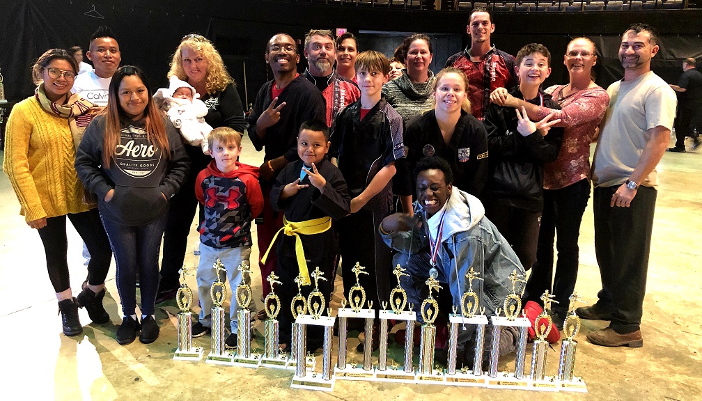 Competitors, family, and Master Anne posing in front of trophies.