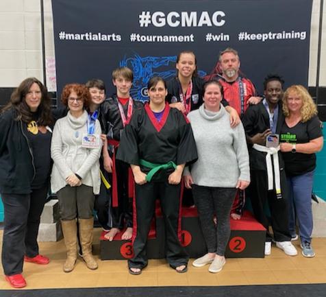 Competitors, family, and Master Anne posing in front of flag.